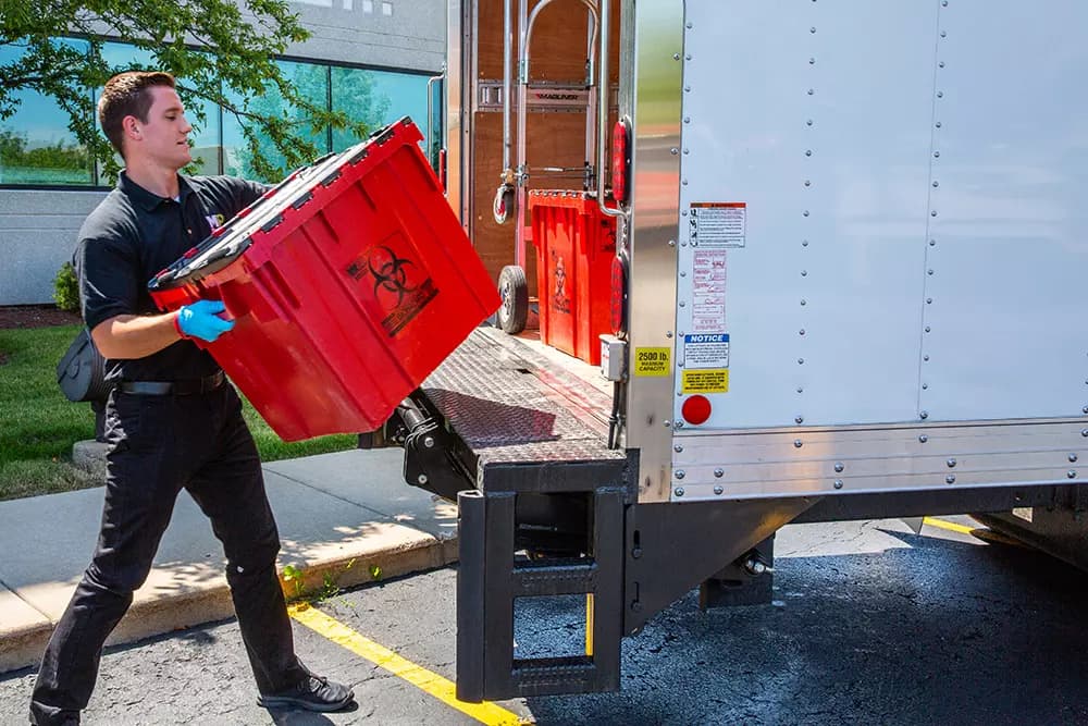 MedPro Disposal driver loading a regulated medical waste container onto a truck