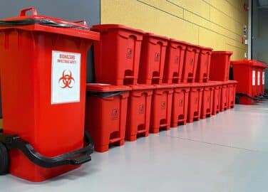 Containers of medical waste sit in a row awaiting pickup & disposal.